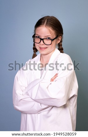 pretty young girl with black glasses and white work lab coat in front of blue background