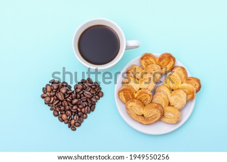 Cup of black coffee, cookies in the shape of hearts, grains of coffee in the shape of a heart on a blue background, copy space, top view. Morning coffee for loved ones.