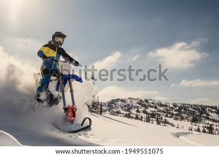  Rider on snowbike in beautiful mountain landscape, puffs of snow behind motorcycle