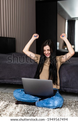 Young woman finished her homework on the floor using a laptop with win gesture happy and holding hands up