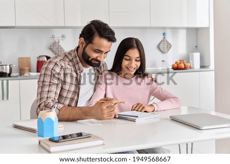 Happy indian father helping school child hugging teen daughter studying at home. Young dad explaining kid teenage daughter learning in kitchen together, doing homework during homeschooling time.