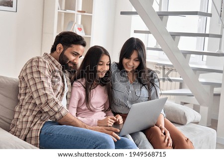 Happy indian family couple with child daughter using laptop computer at home. Smiling parents and teen kid bonding watching streaming online tv or doing ecommerce shopping together sitting on sofa. Royalty-Free Stock Photo #1949568715