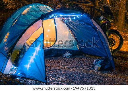 Big blue tent, glows. garlands and lighting in the camp. Camping. Motorcycle and hammock. Parking in the woods. Travel and vacation. Equipment for tourism. Marmore, Italy