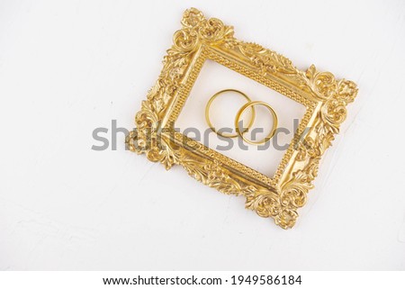 Two golden wedding rings close up with wooden picture frame on white background. Wedding invitation card concept. 