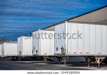 Team of professional freight commercial dry van semi trailers without industrial big rig semi trucks standing at row on business parking lot loading cargo at warehouse dock gates Royalty-Free Stock Photo #1949589004