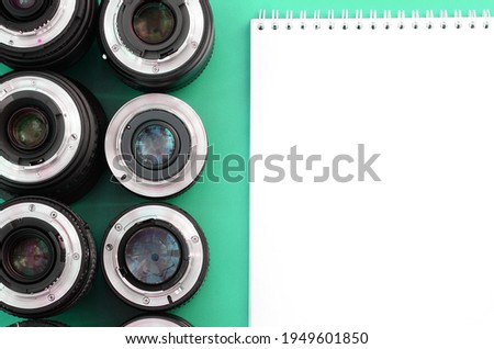 Several photographic lenses and white notebook lie on a bright turquoise background. Space for text
