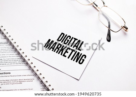 Business concept. Notebook with text DIGITAL MARKETING sheet of white paper for notes and glasses in the grey background