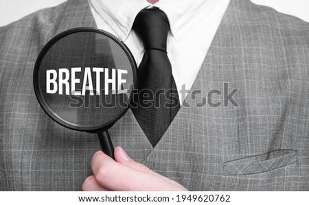 Businessman with magnifying glass on the white background. BREATHE sign