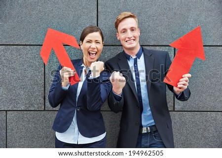 Two happy business people cheering with big red arrows pointing up