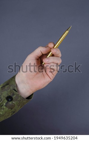 Man in camouflage uniform is holding pen against gray background. Middle-aged man's hand with a gold-colored metal pen. Contract signing, army theme.