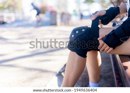 Close up Woman surf skate board putting on knee protector pads on her arm and wearing wrist guards. On morning young women putting protective guard before play extreme surf skate board.