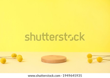 Round wooden podium on beige and yellow background with dried flowers for product presentation. Front view. Copy space.