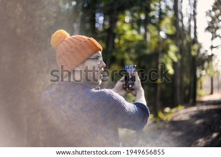 nerdy man with orange hat in the sunny spring Scandinavian forest with phone taking pictures of nature