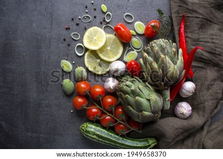 Colorful photo of fresh vegetables on a table. Cherry tomatoes, artichokes, lemon slices, leeks, pepper, zucchini and green almonds top view photo. Gray textured background. Healthy eating concept. 