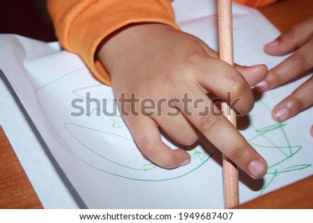 A 3-year-old boy holding a pencil in his hand.