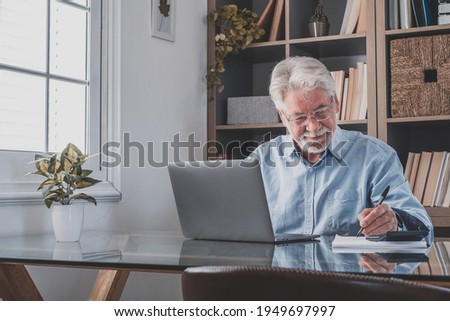 Happy old caucasian businessman smiling working online watching webinar podcast on laptop and learning education course conference calling make notes sit at work desk, elearning concept Royalty-Free Stock Photo #1949697997