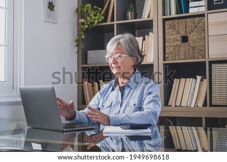 Happy old caucasian businesswoman smiling working online watching webinar podcast on laptop and learning education course conference calling make notes sit at work desk, elearning concept