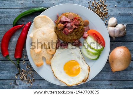 Fried rice is a very popular menu in Indonesia. This menu is even more delicious with sausages, eggs, crackers and vegetables served on white plates