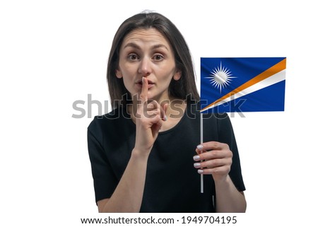 Happy young white woman holding flag of Marshall Islands and holds a finger to her lips isolated on a white background.