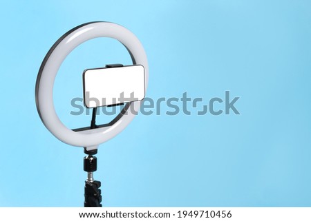 Modern tripod with ring light and smartphone on light blue background. Space for text