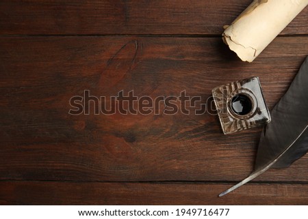 Feather pen, inkwell and parchment scroll on wooden table, flat lay. Space for text Royalty-Free Stock Photo #1949716477