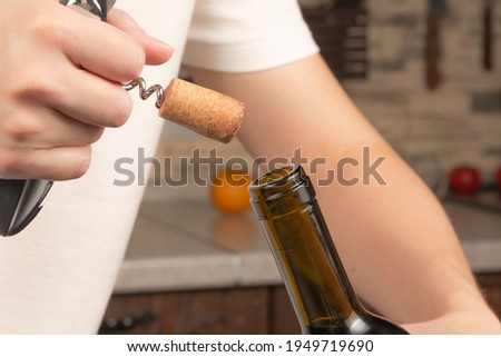 female hands open a bottle of dry red wine with a corkscrew on the background of the kitchen. selective focus. close-up