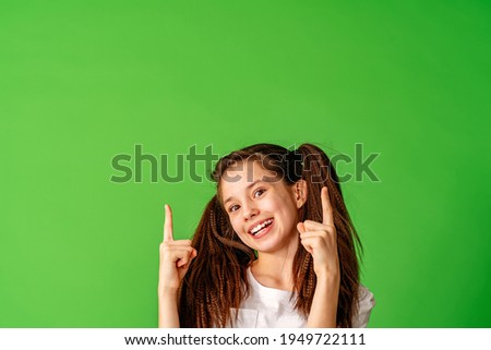 cheerful, happy pre-teen girl points her finger up, copying the place for the text. A smiling, enthusiastic teenager in a white T-shirt is showing off. Advertising concept. Copy space