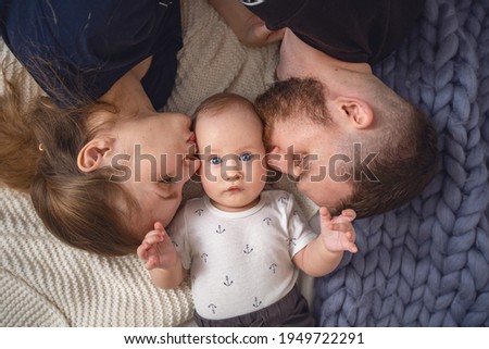Loving parents, father and mother kiss their beloved child on the cheeks, lying on the bed at home. Happy parenthood. Close-up.