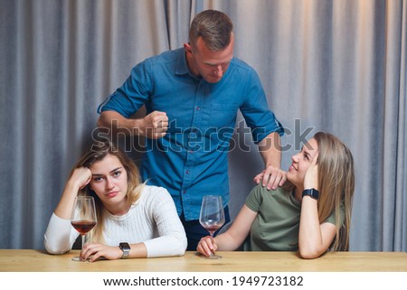 Domestic violence. A young man swears at two girls. They drink alcohol while sitting at the table. Alcoholism of young women