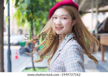 Asian beautifu lady with bronze hair wears red cap and turns to face on the street background.