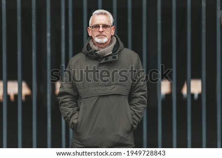 Closure in oneself. Senior man with gray hair stands against the background of jail. Confusion of thoughts, depression.