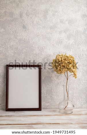 Brown wooden frame mockup with dried hydrangea in glass on gray concrete background. Blank, vertical orientation, still life, copy space.