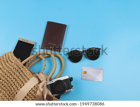 Top view or flat lay of traveling accessories with grey credit card in woven bag on blue background. Traveling concept.