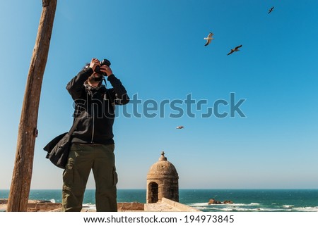 Handsome man with dreadlocks taking a photograph at a seaside during vacation