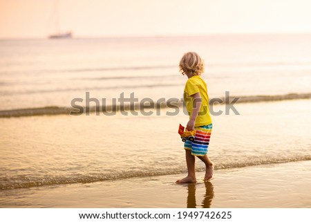 Child playing on ocean beach. Kid jumping in the waves at sunset. Sea vacation for family. Little boy running on exotic island during summer holiday. 