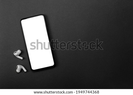 Mobile phone with empty screen and earphones on black surface. Wireless earphones, mobile phone on black background, top view. copy space White wireless bluetooth headphones and smartphone Royalty-Free Stock Photo #1949744368