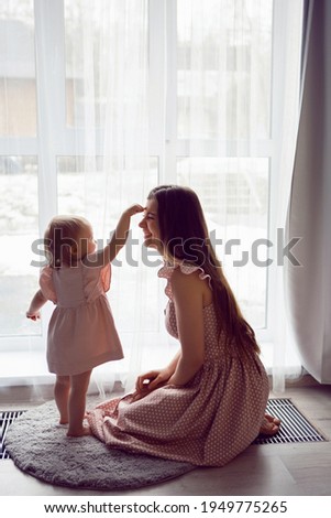 woman with a girl child in pink dresses stands at a large window