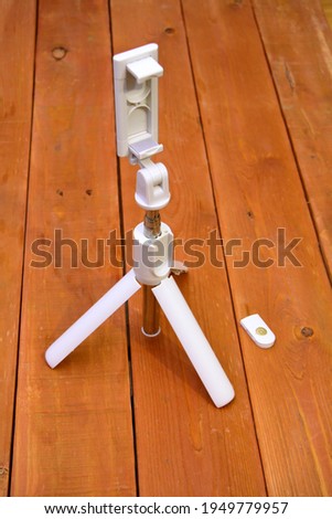 Selfie stick. for a smartphone. The material is white. with control panel. On a wooden background