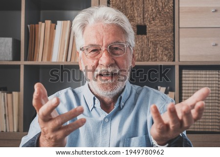 Head shot portrait confident old businessman coach wearing glasses looking at camera and talking, mentor speaker holding online lesson, explaining, sitting at wooden work desk in modern cabinet Royalty-Free Stock Photo #1949780962