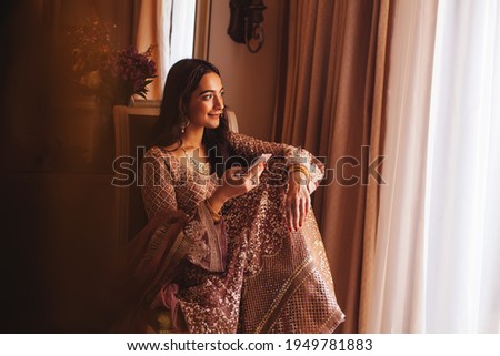 Rich beautiful Indian woman in luxury ethnic clothes using her phone in a 5 star hotel room. Filtered portrait in muted colors, film photography style Royalty-Free Stock Photo #1949781883