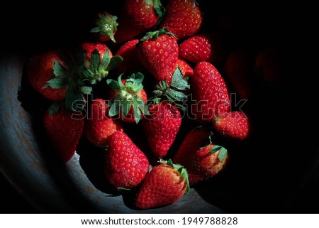 Plate full of strawberries, in vintage bowl, on blurred black background 