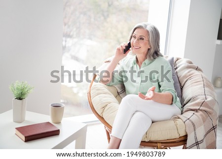 Photo of pretty positive person sit on chair near window speak phone have good mood weekend indoors