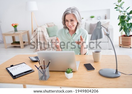 Photo of cheerful friendly lady sit behind desk toothy smile look laptop speak video chat hands explaining house indoors