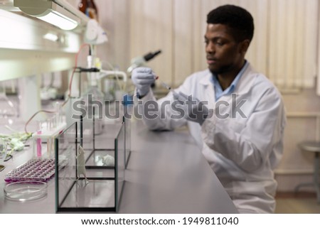 Image of experimental little mouse in glass container with scientist preparing an injection for them in the lab