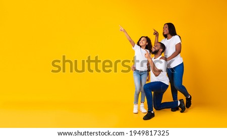 Special Offer. Cheerful African American Family Of Three People Looking Aside And Pointing Fingers Up And Aside At Free Copy Space On Yellow Background, Presenting Empty Place For Advert, Banner