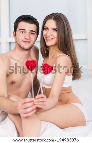 love valentine day couple holding red heart young lovely together lying in a bed, happy smile looking at camera, concept hearts flying around