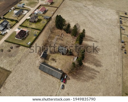 Drone photo of a propery in the middle of the field. Old farmstead which now is surrounded by new fancy realestate developments. Image taken from above. Early spring, no leaves, lifeless nature