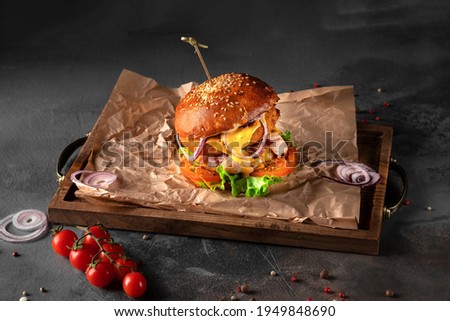 big american burger on a black background. cutlet with cheese, tomato, onion and salad on a wooden tray, side view
