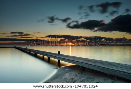 Wooden jetty in a calm lake at sunset with ominous clouds over the horizon