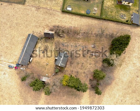 Drone photo of a propery in the middle of the field. Old farmstead which now is surrounded by new fancy realestate developments. Image taken from above. Early spring, no leaves, lifeless nature